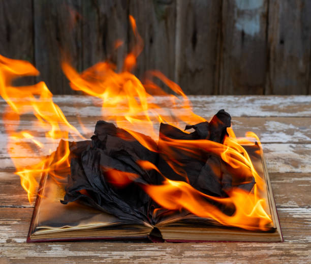 istock An open book burning in a fire on an old wooden table in close-up 2203605569