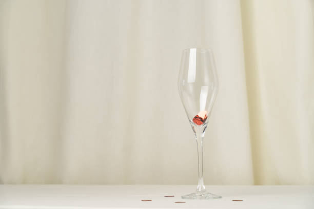 Wine glass with heart confetti on cream background. Minimalist holiday photo for Valentines