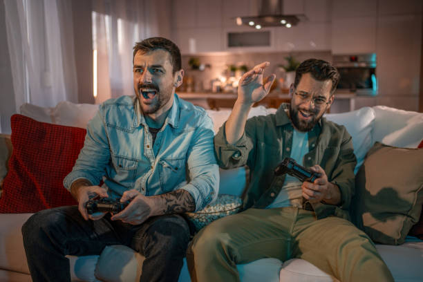 istock Two young men playing video games at home on the couch 2203607413