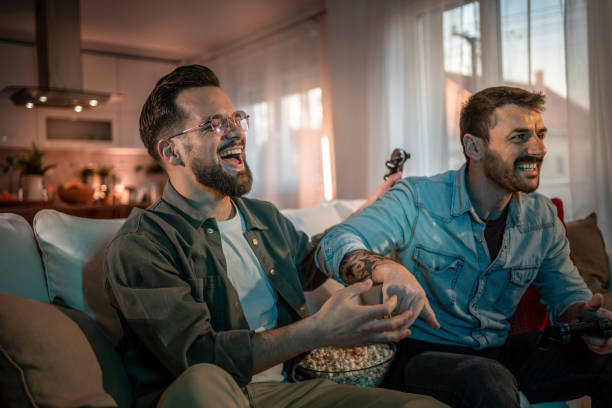 istock Two friends laughing while playing video games and eating popcorn at home 2203607506