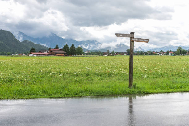 Hohenschwangau, Germany - July 25, 2017: A tranquil rural landscape with a signpost directing to local destinations, set against a backdrop of fields and a cloudy sky.