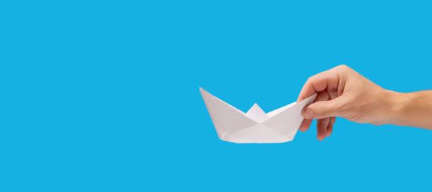 istock Paper boat in hand isolated on blue background. 2203609029