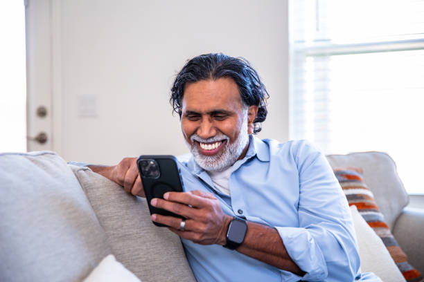 istock Mature Indian man at home smiling using his smartphone on couch 2203612162