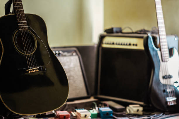 A photograph of a music studio featuring an acoustic guitar and an electric bass in the foreground. In the background, amplifiers and effect pedals complete the scene, emphasizing the atmosphere of creativity and music production. The absence of people highlights the connection between the instruments and music in its purest form
