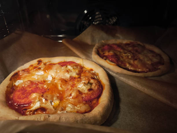 Two delicious mini pizzas with tomato and melted cheese are baking in a hot oven on baking paper