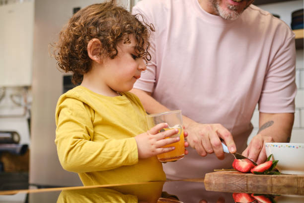 istock Father slicing strawberries while son drinks orange juice in kitchen 2203614751