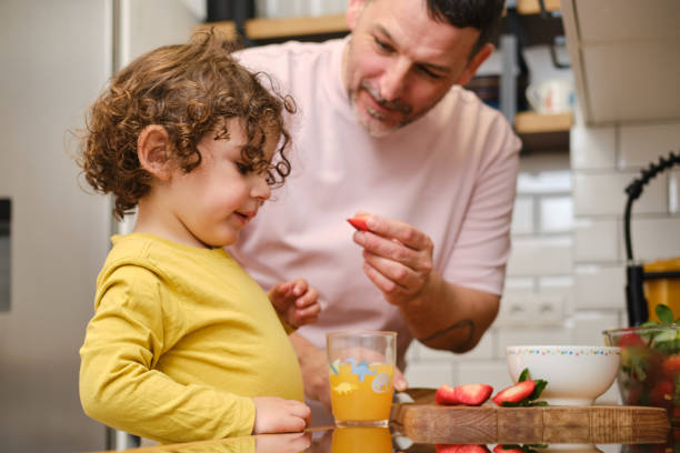 istock Father feeding his child with strawberries in the kitchen 2203614761
