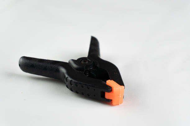 istock A black plastic spring clamp with orange tips sits on a white surface, ready for holding or securing objects. 2203615111