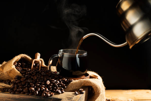 istock Pour black coffee into a coffee cup There are roasted coffee beans on the table. with a black background and dark colors 2203617256