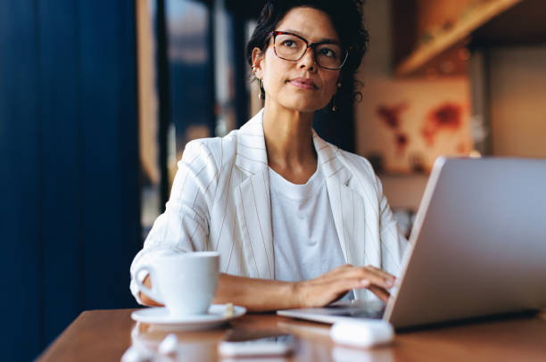 Professional woman working on laptop in a cafe, thinking deeply