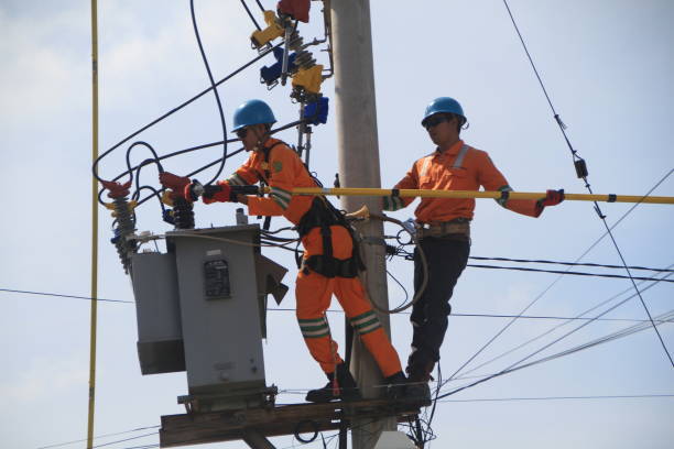 Utility electrical worker uses bucket truck to fix an electrical transformer atop wooden pole against