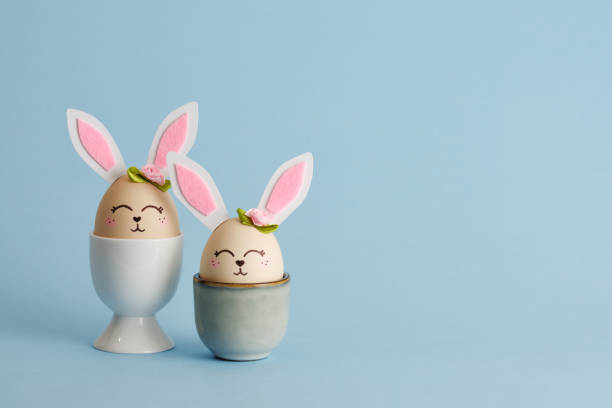 istock Cute Easter bunny shaped eggs in egg holders on blue background. Place for your text 2203636700