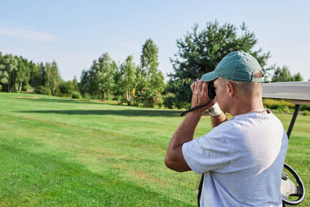 istock Golfer monitors the results of his shot with binoculars while standing on a green golf course under bright blue skies 2203637395