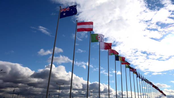 istock Low angle view of multiple flags on poles over blue sky with clouds background 2203642240