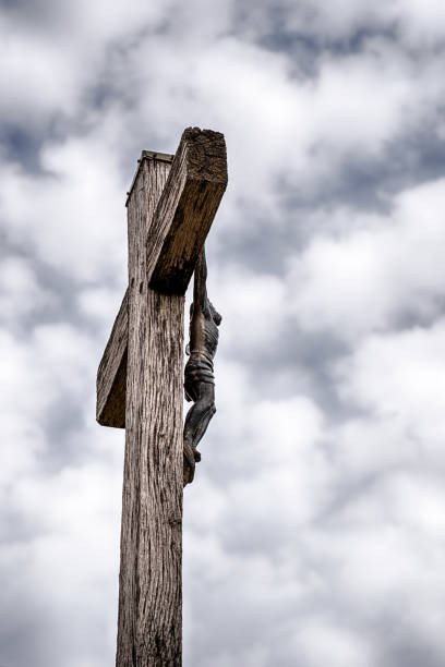 A wood crucifix with Jesus Christ in the outdoor cemetery at St. Pantaleon, France is isolated against a cloudy sky.