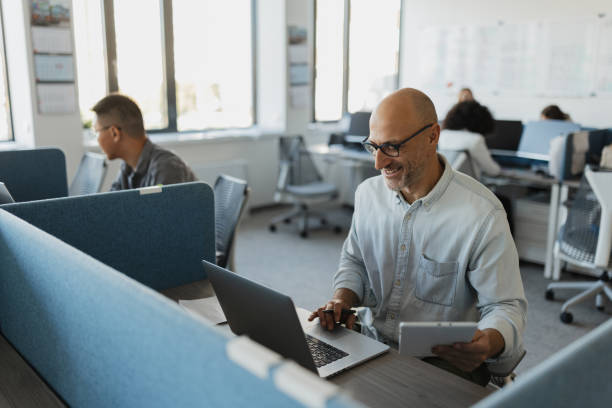 istock Cheerful man with tablet and laptop at desk 2203643294