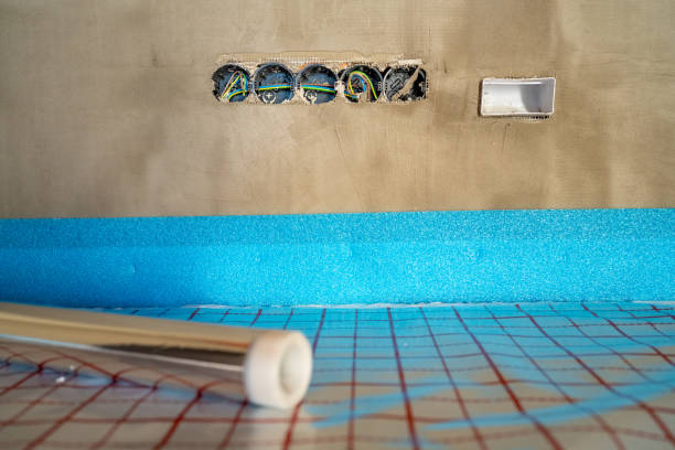 Installing underfloor heating foil with insulation on concrete floor and mounting electrical outlets in a wall during renovation or construction work in a house