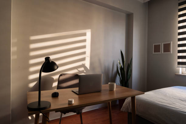 Cozy home office setup in bedroom with blinds casting shadows
