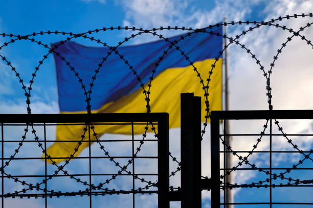 istock Ukrainian flag waving behind barbed wire fence under blue sky 2203673092