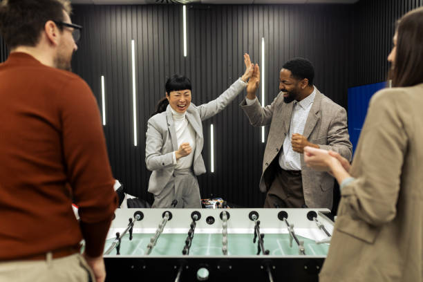 Group of business people , colleagues having fun playing table football at the office, having break from work