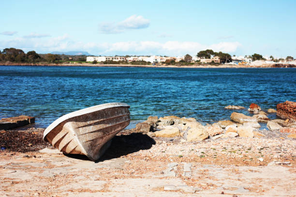 abandoned white boat on the seashore against blue water under the scorching sun an old boat lies on the rocks near the sea