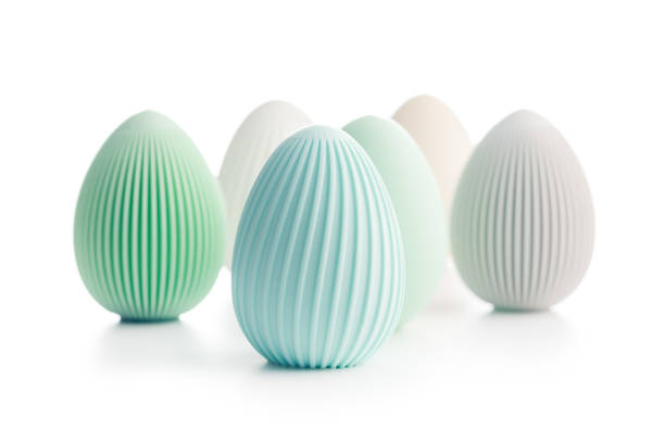 A close-up shot of a beautifully decorated blue and green Easter eggs, resting on vibrant green grass. A blurred green egg is visible in the background, adding depth to the composition.