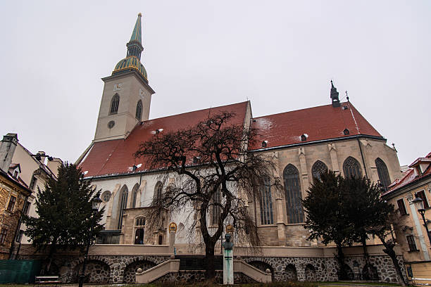 February 20, 2025 Bratislava, Slovakia. St. Martin's Cathedral, located in Bratislava, Slovakia, stands tall against a cloudy winter sky, its red tiled roof dusted with snow, bare trees framing its gothic architecture