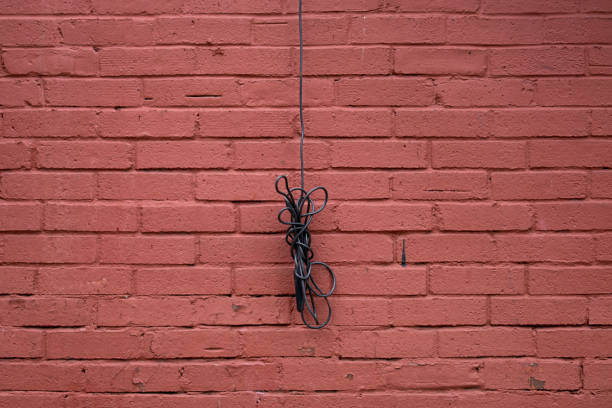A black cord is hanging from a brick wall. The cord is tangled and twisted, and it is hanging from the wall. The image has a somewhat eerie and mysterious mood