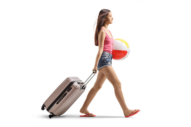 istock Teenage girl with a beach ball walking and pulling a suitcase 2203698968