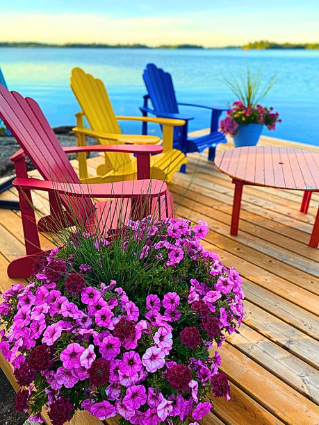 Adirondack chairs on a dock with colorful flower pots. Lakeside view of a lake in Kingston, Ontario