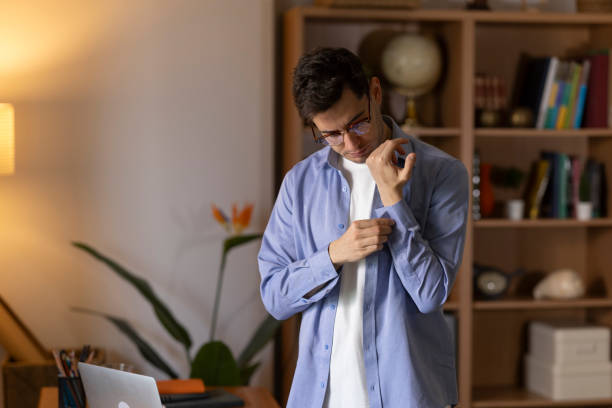 Young adult businessman buttoning his shirt sleeve while getting ready for work at home office