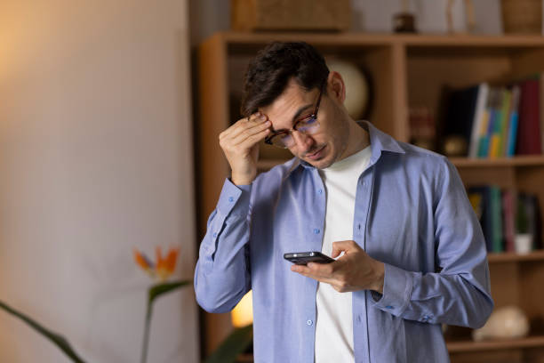 istock Young man holding his head while reading bad news on his mobile phone 2203721917