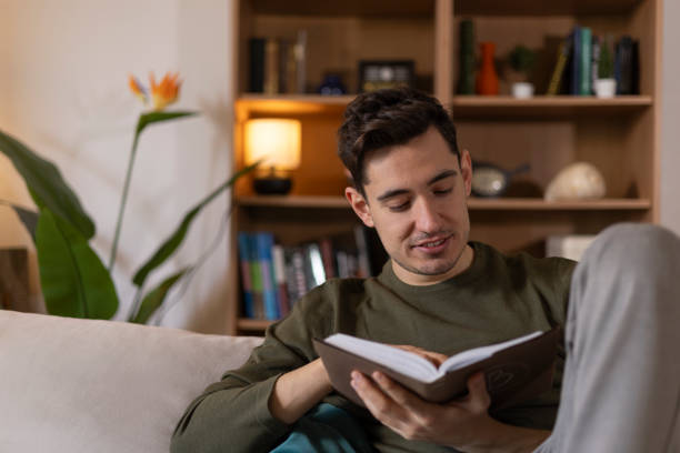 istock Young man enjoying his leisure time reading a book while relaxing on a comfortable sofa in his living room 2203722142