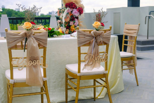 View of bride and groom chairs at wedding table setting for solemnisation ceremony, beautiful outdoor event setting at a rooftop overlooking city. Pretty flower bouquets on table. Rooftop wedding.