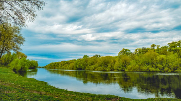 Beautiful spring green landscape with  flowing river and  fluffy clouds. Beautiful nature on spring. No people. Photo of a  summer landscape with a cloudy skies.