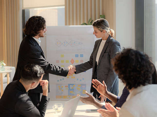 istock Business Meeting Whiteboard Presentation Office Strategy Discuss , Business team shows unity by shaking hands in sunny conference room. Group of people holding hands and representing the concept of friendship and teamwork. 2203735340