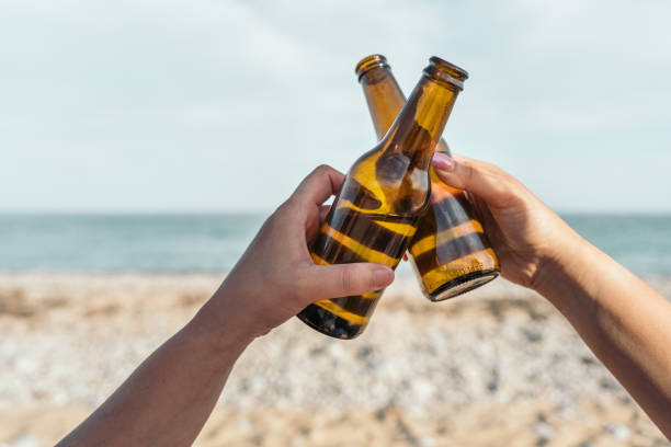 istock Hands clinking glass beer bottles together on a sunny beach 2203735482