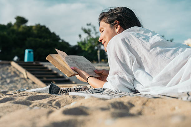 istock Young woman relaxing on the beach reading a book 2203737702