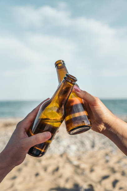 istock Hands clinking glass beer bottles together on a sunny beach 2203737847