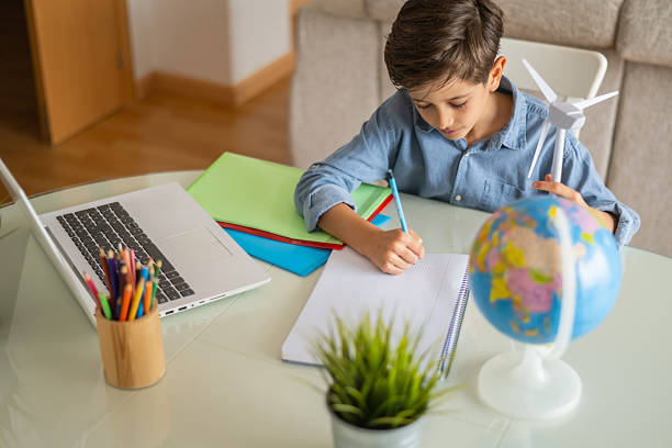 istock Elementary age schoolboy is learning about renewable energy, observing a model wind turbine and a globe at his desk at home, with a laptop and colored pencils nearby 2203738594