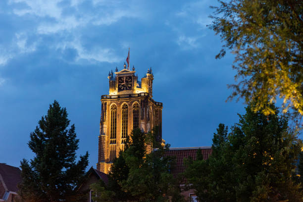 A majestic Gothic church under a dramatic cloudy sky. The intricate brickwork, towering windows, and clock tower reflect its historic architecture and timeless grandeur.