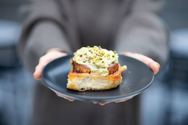 istock Close up of hands holding plate with cinnamon roll. 2203743337