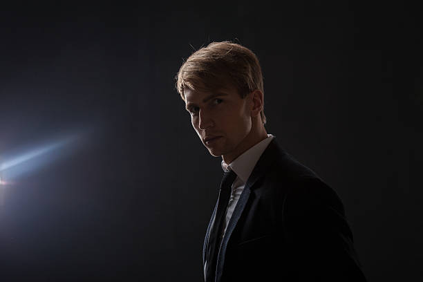 istock In a dark studio, a man in a black suit and white shirt stands in profile. 2203748478