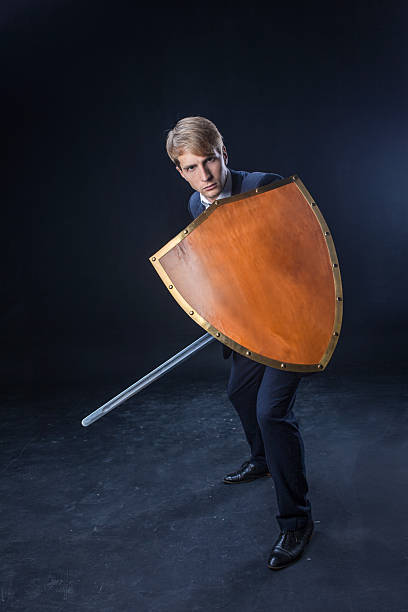 istock man in a navy suit stands poised with a sword and shield 2203748722