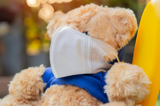 istock Brown Teddy bear with mask sitting alone at the park. Sick concept. 2203750634
