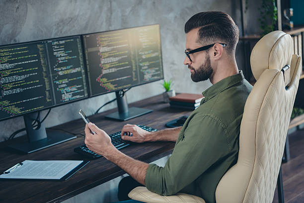 istock Photo of smart clever young man wear green shirt spectacles coding computer program typing modern device indoors workshop workstation 2203754834