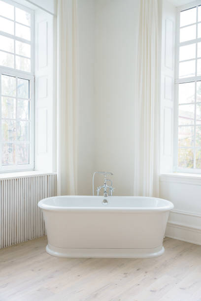 istock Minimalist white bathroom with a freestanding bathtub near large windows, featuring soft natural light and an elegant, serene atmosphere. 2203758358