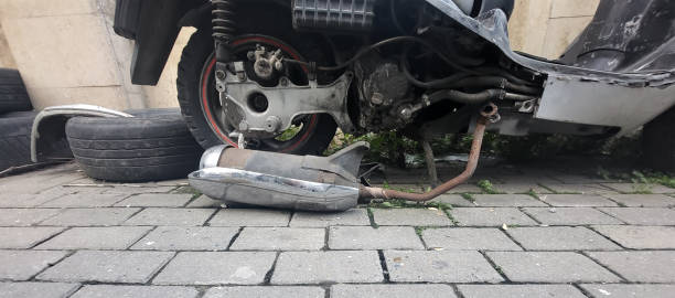 Burnt motorcycle frame after a fire on a city street. Charred metal, melted parts, and signs of destruction near a stone wall and iron fence. High quality photo