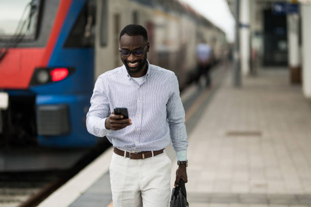 istock Cheerful black businessman using smart phone after arriving on railway station. 2203762354