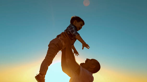 istock Caucasian Father Joyfully Lifting Son Against Sunset Sky 2203778181